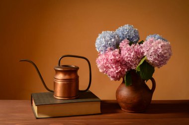 Durgun bir hayat, seramik bir vazoda çiçekler, ahşap bir masada kitap ve bakır kaplar.