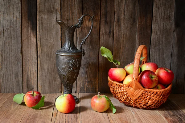 Apples in a wicker basket with a antique metal jug — Stock Photo, Image