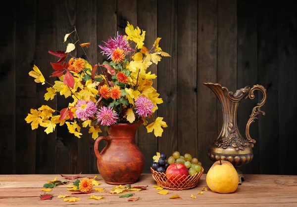 Flowers and leaves in a metal jug and fruit — Stock Photo, Image