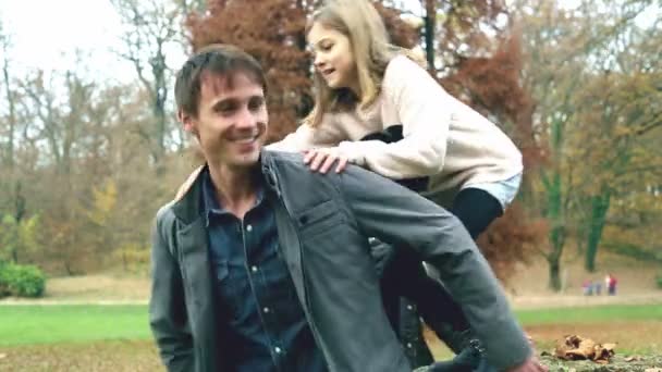 Flickan hoppar på pappas tillbaka i parken — Stockvideo