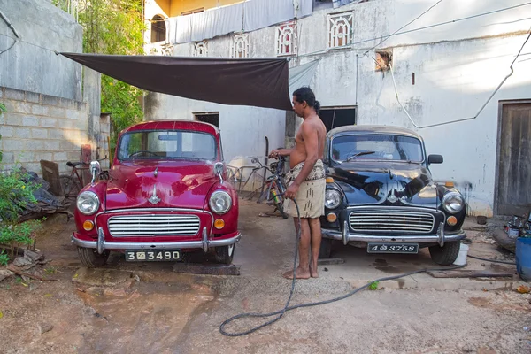 Local man washing two Morris Minor cars in the yard with water hose — Stock Photo, Image