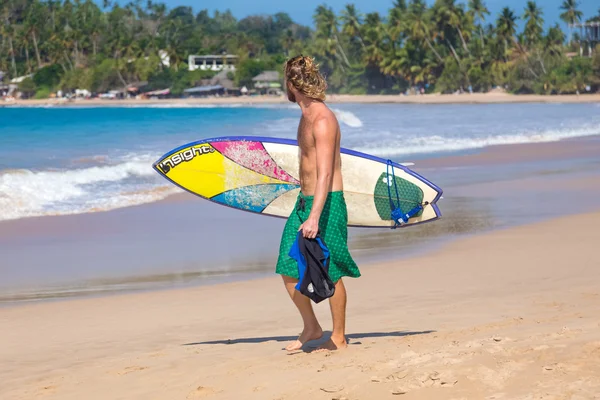 Jonge man loopt op zandstrand surfplank uitvoering. — Stockfoto