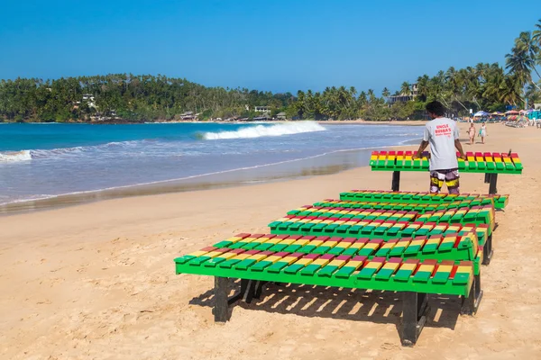 Travailleur local mettant des chaises longues en bois coloré sur la plage — Photo