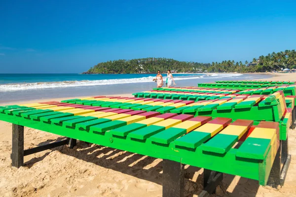 Local worker putting colourful wooden deck chairs on beach — Stock Photo, Image