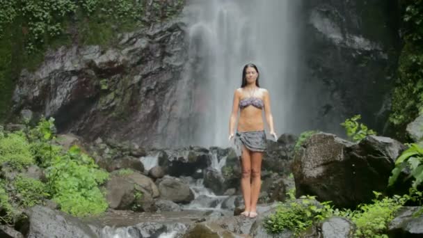 Женщина стоит под водопадом — стоковое видео