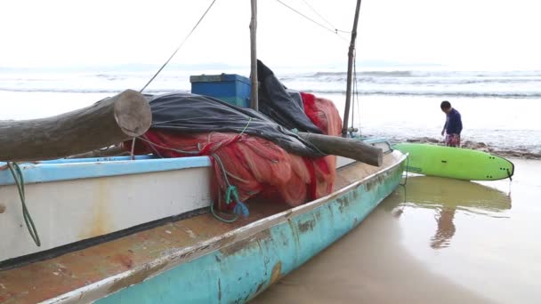 Boot am Strand in Weligama mit vorbeifahrenden Surfern — Stockvideo