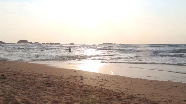 Golven spatten van het strand en mensen krijgen in de Oceaan — Stockvideo