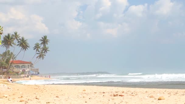 Волны брызгают по пляжу, пока люди проходят мимо — стоковое видео