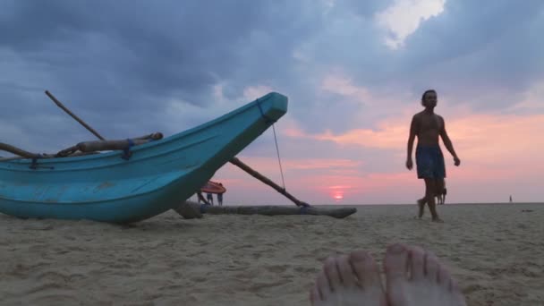 路过的人在日落时分在沙滩上小船 — 图库视频影像
