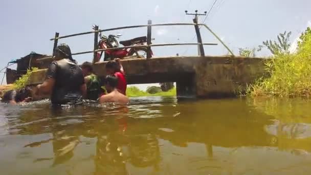 Cámara bajando río viendo a los lugareños nadando y pasando por debajo del puente . — Vídeos de Stock