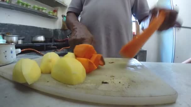 Homem cortando cenouras e batatas com uma faca na cozinha . — Vídeo de Stock