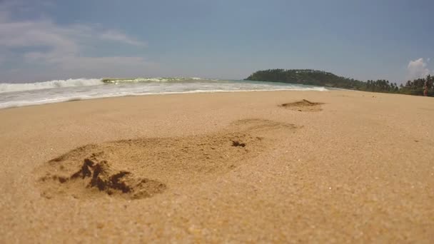 Fale zmywania na odbitki stóp na piasku na plaży w tropikach — Wideo stockowe