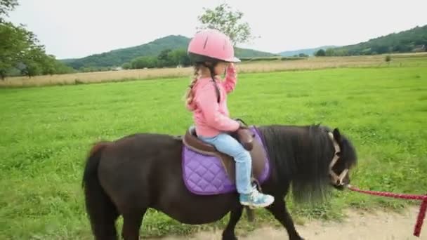 Маленькая девочка едет на пони в сельской местности — стоковое видео