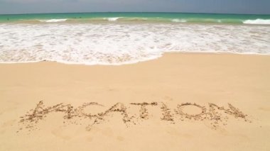 Kum plaj üzerine yazılmış sözcük tatil kapsayan dalga okyanus