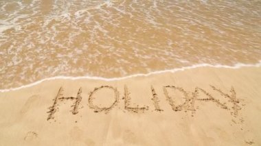 Kum plaj üzerine yazılmış sözcük tatil kapsayan dalga okyanus