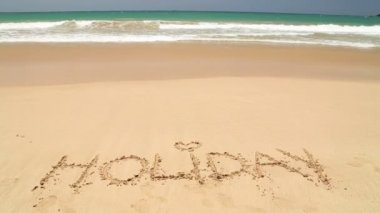 Kum plaj üzerine yazılmış sözcük tatil kapsayan dalga okyanus