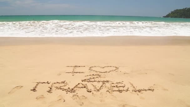 Ocean wave approaching words I love to travel written in sand on beach — Stock Video