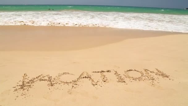 Океанічна хвиля наближається до слова відпустка написана в піску на пляжі — стокове відео