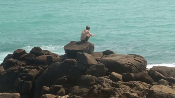 Man går på ett stort stenblock på en strand — Stockvideo