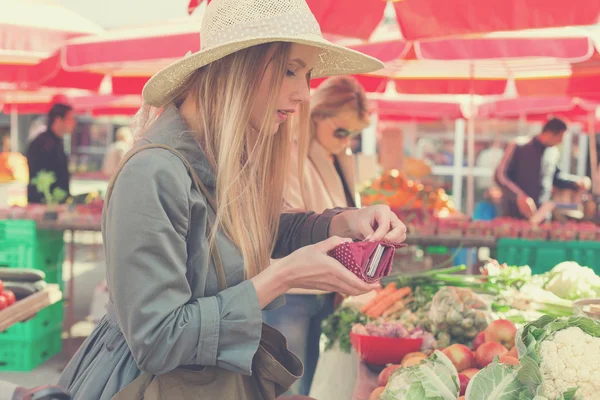 Attraktive blonde Frau mit Strohhut bezahlt Gemüse auf dem Marktplatz. — Stockfoto