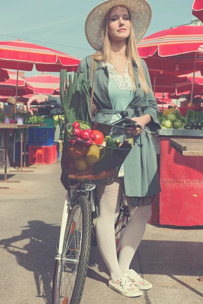 Attractive blonde girl with straw hat and bike on Marketplace. — Stock Photo, Image