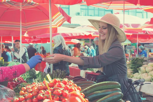 Attractive blonde woman with straw hat paying vegetables on  marketplace. — Stock Photo, Image