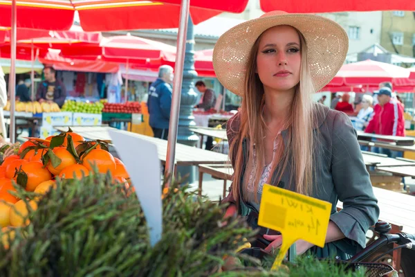 Aantrekkelijke blonde vrouw met stro hoed en fiets op Marketplace. — Stockfoto