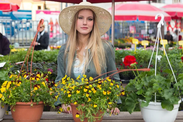 Attractive blonde woman with straw hat posing on flower marketplace. — Stock Photo, Image