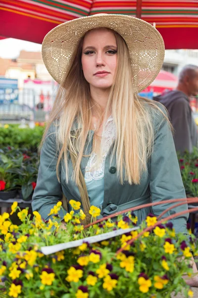Hasır şapka çiçek pazarı üzerinde poz çekici sarışın kadınla. — Stok fotoğraf