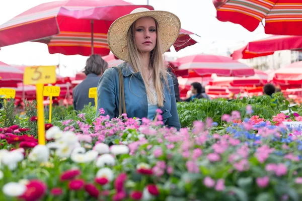 Attractive blonde woman with straw hat posing on flower marketplace. — Stock Photo, Image