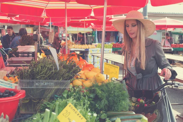 Atraktivní blondýnka se slamákem a kolo na tržišti. — Stock fotografie