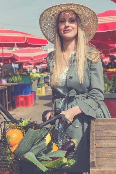 Atractiva mujer rubia con sombrero de paja y bicicleta en el mercado . —  Fotos de Stock