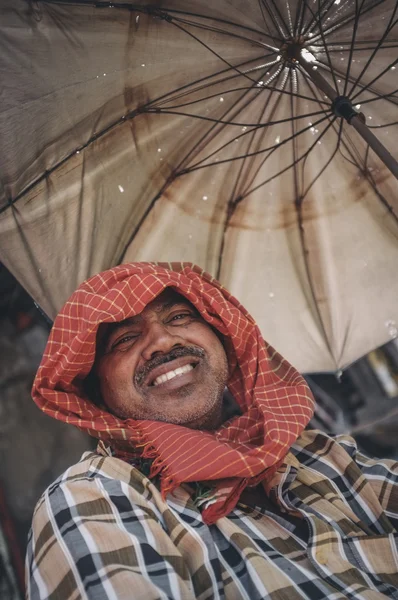 Hombre sonriendo y sentado bajo una sombrilla — Foto de Stock