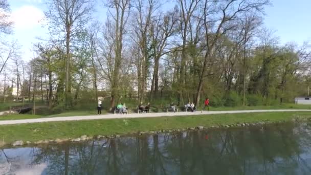 Вид з повітря на людину, що біжить біля озера, з людьми, що сидять на лавках . — стокове відео