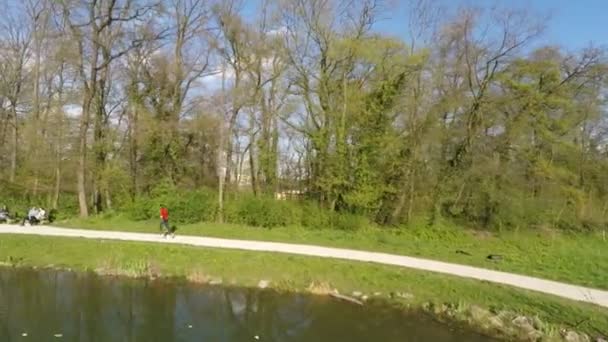 Vista aérea do homem que corre junto ao lago, com pessoas sentadas em bancos . — Vídeo de Stock