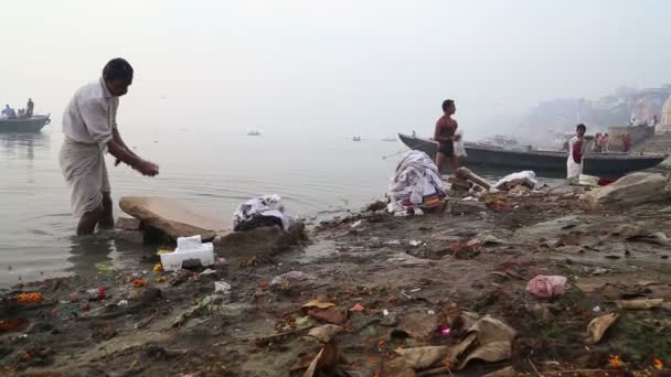 Мужчины стирают белье на грязном берегу — стоковое видео