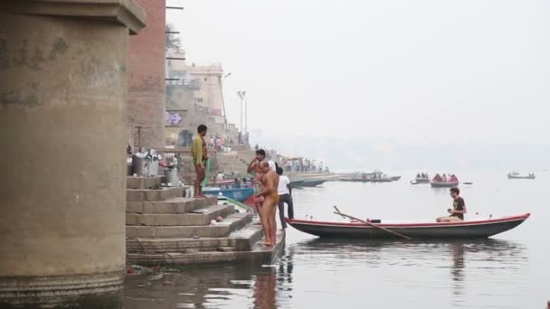 Men standing on dock of Ganges after bath, with man in boat on river. — Stock Video
