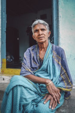 woman sits in sari in-front of home