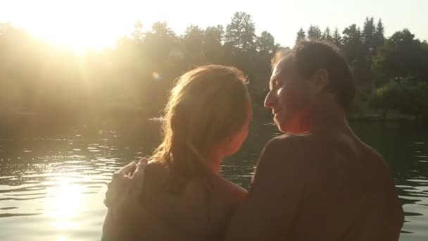 Пара, сидящая рядом с рекой на закате — стоковое видео