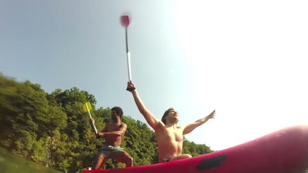 Dos amigos masculinos se divierten saludando con paletas en una canoa — Vídeos de Stock