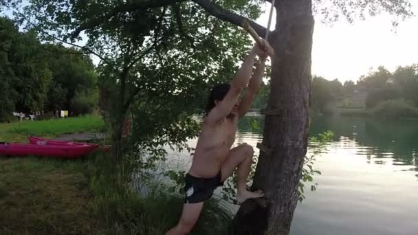 Man jumping from swing into river — Stock Video