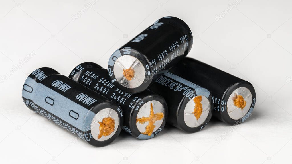 Aluminum electrolytic capacitors with failure from disuse on a white background. Pile of electrical condensers with leaked electrolyte fluid. Damaged passive electronic components. E-waste. Side view.