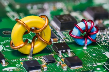 Yeşil devre kartında iki toroid indüktörü ve elektronik transistörler. Bilgisayar ana tahtasının gömülü gerilim dönüştürücüsünde PCB 'de güzel sarı ya da mavi indüksiyon bobini. Yarı iletkenler. Teknoloji.