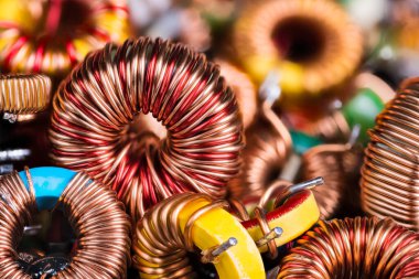 Toroidal electronic inductors on heap in electrotechnical background. Closeup of beautiful induction coils with copper wire winding on magnetic ferrite core. Colored electrical engineering components. clipart