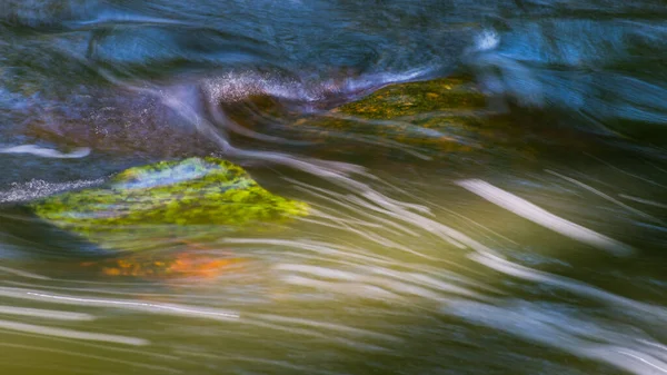 苔むした石の上を流れる渓流の自然背景 白い流線に動きのブレがある緑と青の動的波状水面 速い実行中の迅速なクリークベッドのクローズアップ — ストック写真