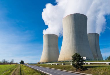 Mavi gökyüzü arka planında su buharı olan nükleer santral soğutma kuleleri. Çevredeki modern üretim istasyonuna bir yol ve yeşil çimlerin üzerinde buhar boruları ile yakın plan. Çevre. Temelin, Çek Cumhuriyeti.