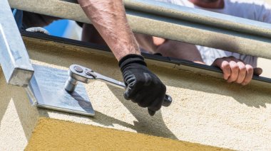 Cırtlak soket anahtarıyla sürgülenmiş. Metal yapıyı bina duvarına bağlamak. Çelik iskelet betona bağlanıyor. Balkon ya da teras koruma korkulukları döşeyen işçiler. Alt görünüm.