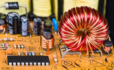 Elektronik bileşenleri olan basılı devre kartındaki toroidal veya silindirik indüktörler. Manyetik çekirdek bobinlerinin, mikroçiplerin, dirençlerin ya da kapasitörlerin turuncu PCB detaylarına yakınlaştırılması. Elektrik mühendisliği..
