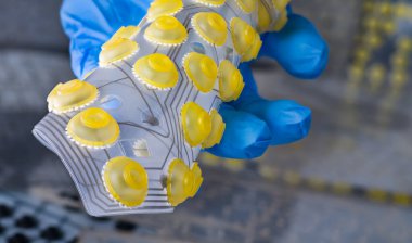 Silikon baskı devre kartı bilgisayar klavyesinin zarında kıvrılmış. Sarı yuvarlak düğmeli plastik esnek PCB tutan mavi eldivenli mühendis eli. Elektronik.