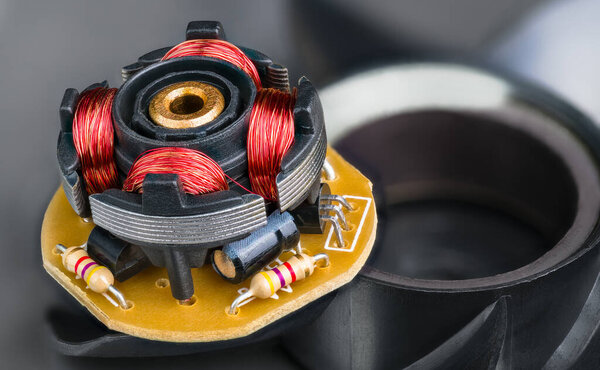 Ротор электронно-коммутируемого двигателя от компьютерного вентилятора. Черные пластиковые лопасти детали. Закрытие медных проволочных обмоток и резисторов, транзисторов или конденсаторов внутри электрической машины. Селективный фокус.